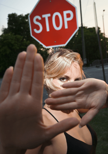 #060: Why Do You Have to Be So Defensive? -Photo of a girl holding her hands up in front of a stop sign representing a wife who feels defensive and might feel attacked by her husband or partner. Our Affair Recovery Program & Couples Therapy services will help you reduce the defensiveness in your relationship or marriage.