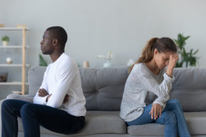 A couple face away from one another on the same sofa. This could symbolize the pain of infidelity PTSD. Contact Idit Sharoni to learn about PTSD from cheating, and how a infidelity recovery program can help with infidelity recovery today.