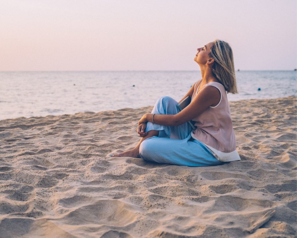 Woman sitting on the beach with her eyes closed and meditating