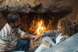 Shows a couple talking and holding hands in front of a fire. Symbolizes how a couples therapist in florida will empower you to learn about your partner's love language.