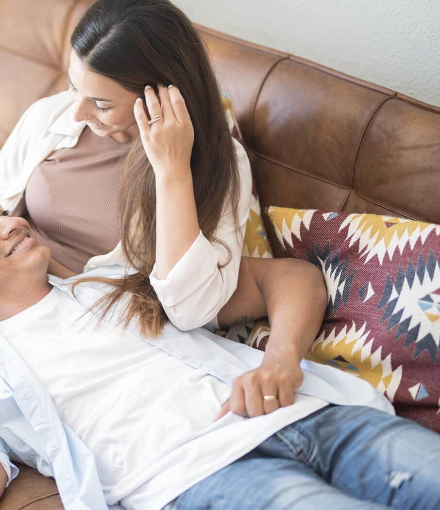 Photo of a couple sitting on a couch smiling at each other. Discover how being vulnerable in your relationship can help you and your partner. Learn more with marriage counseling in Florida.