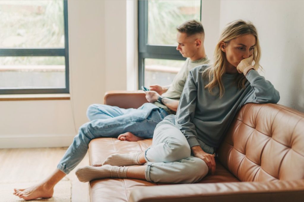 photo of a couple sitting on a couch with their backs to each other they seem upset and not communicating