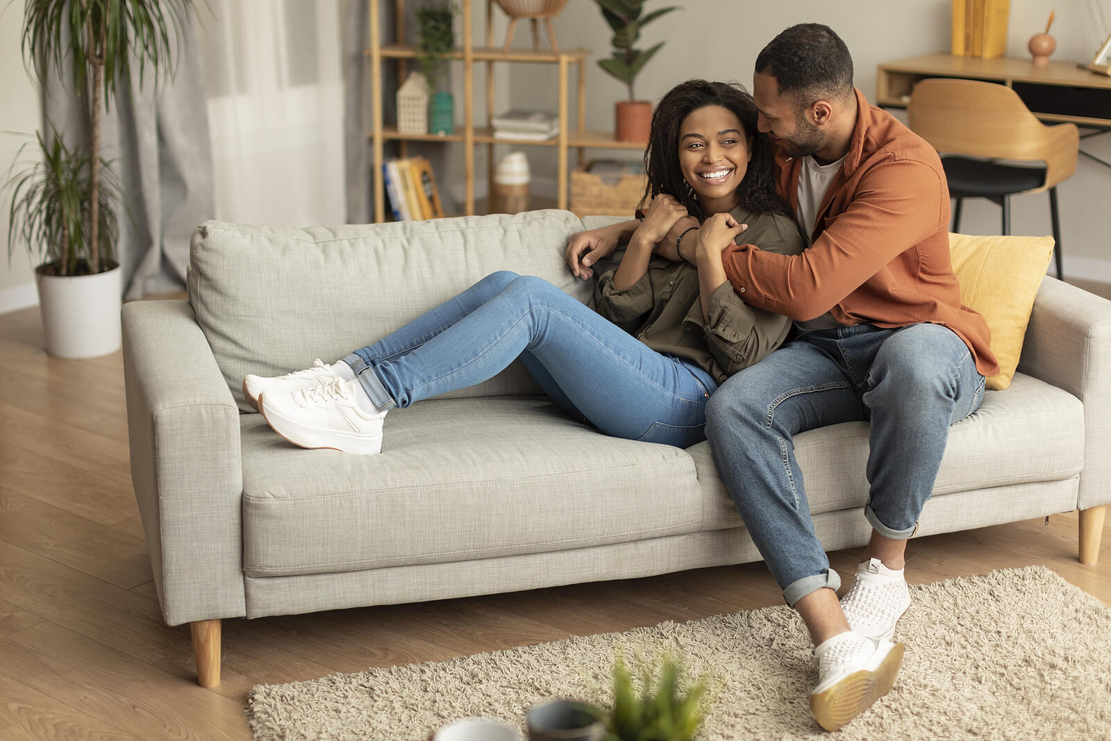 Photo of a couple smiling and sitting on a couch hugging with each other. If you and your partner are struggling to communicate, learn how a communication therapist in Florida can help provide you and your partner with support.