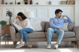 Photo of a couple sitting away from each other on a couch looking upset. This photo represents how relationship trauma can damage a relationship. Discover how marriage counseling in Florida can help you begin to repair your relationship.