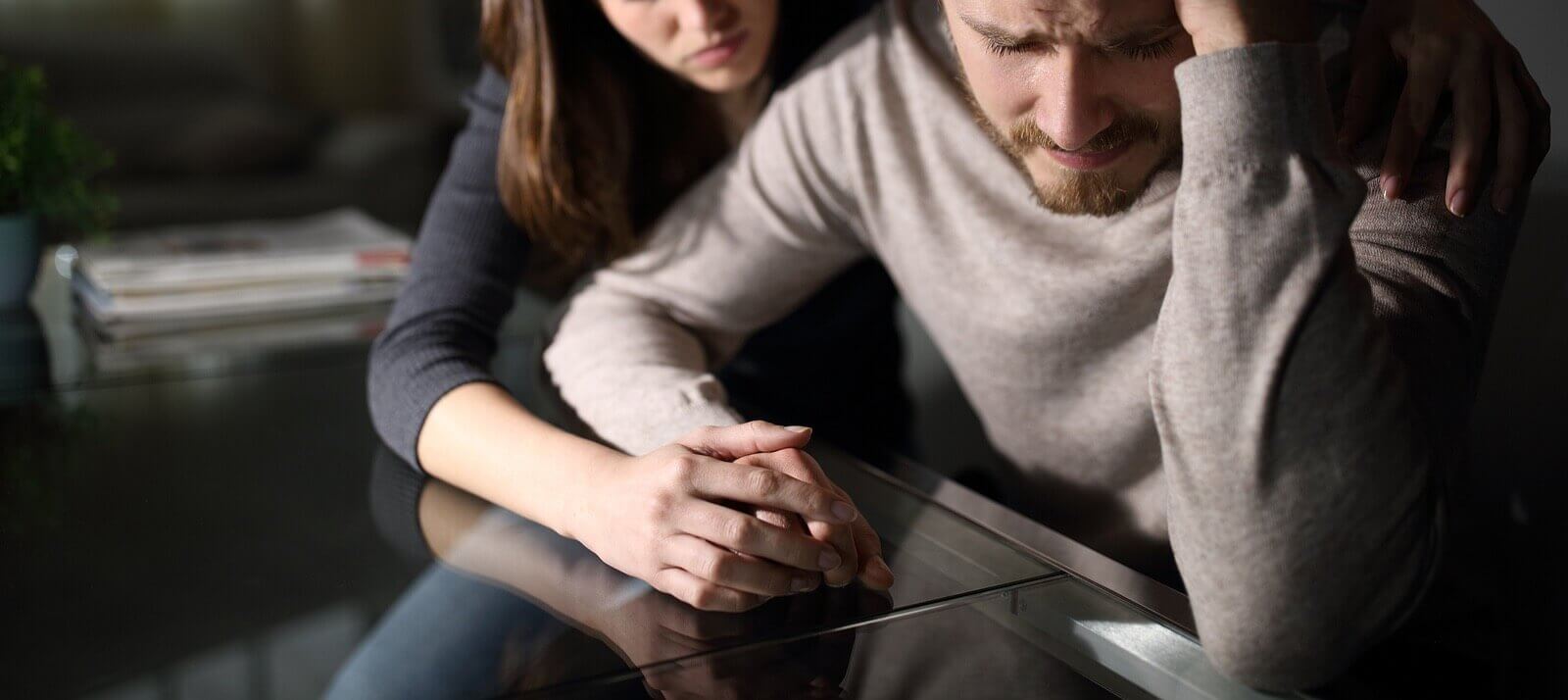 Photo of a sad man with a woman holding his hand and comforting him. Are you and your partner struggling with infidelity? Learn how a infidelity recovery program in Florida can help you find support.