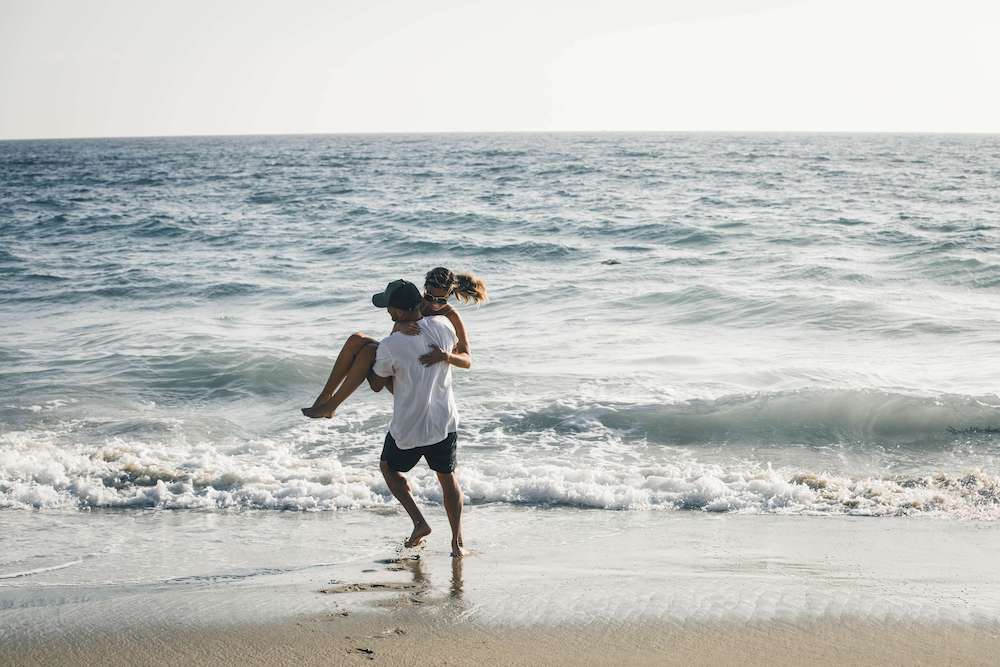 Photo of a happy couple running on a beach during a sunny day. Struggling to overcome conflict with your partner? Learn to effectively communicate with your partner and resolve conflict with the help of couples therapy in Miami, FL.