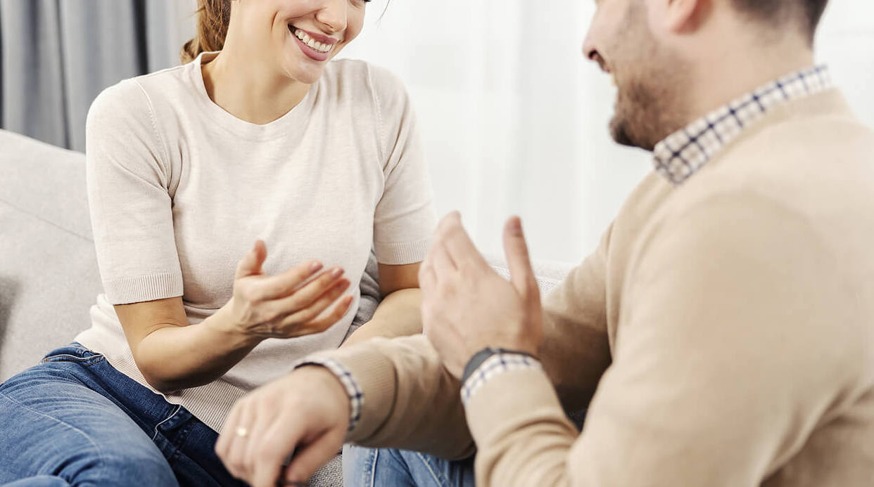 Image of a couple happily chatting on a couch. Discover how couples therapy in Miami, FL can help you work to overcome your communication issues to maintain your intimacy.
