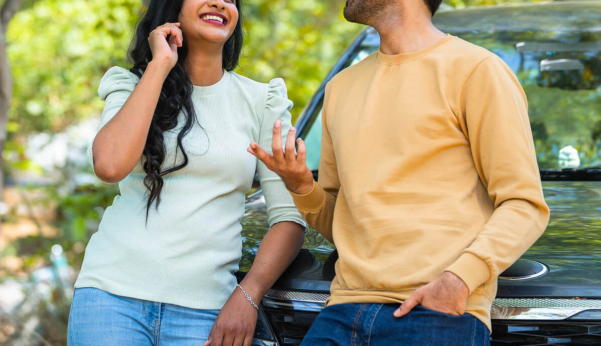 Image of a smiling couple talking and standing outside leaning against a car. Uncover your communication issues with the help of couples therapy in Miami, FL. Work with a couples therapist to reignite the spark and not divorce.