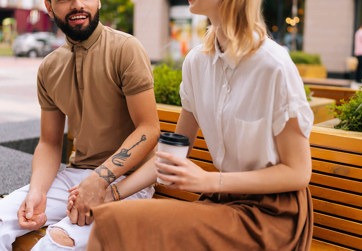 Image of a smiling couple holding hands and sitting on a bench outside. Learn how a couples therapist in Miami, FL can help you and your partner in couples therapy by improving your communication.