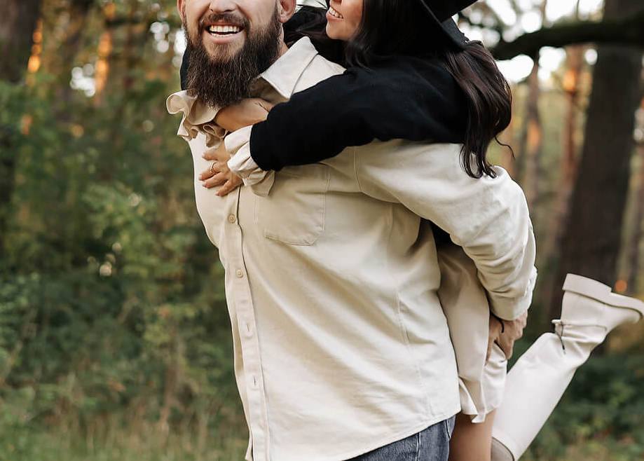 Image of a smiling man carrying a smiling woman on his back in the forest. Learn to overcome your communication issues to help with your intimacy issues with the help of couples therapy in Miami, FL.