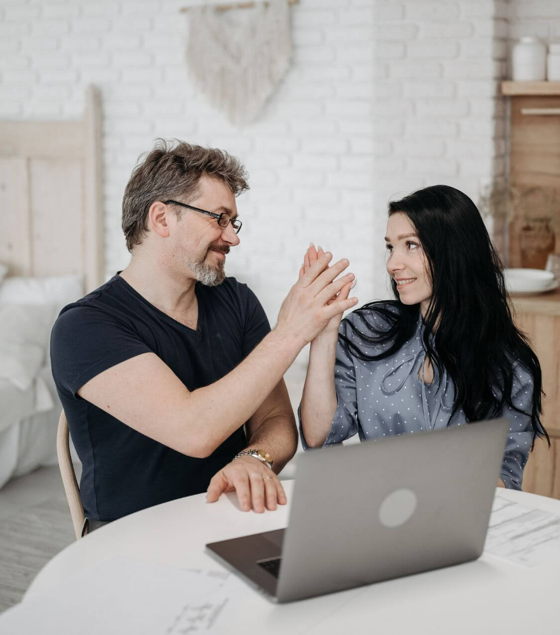 Image of a couple sitting in front of a laptop smiling at each other and high-fiving. Discover how online couples therapy in Miami, FL can help you and your partner connect more intimately.