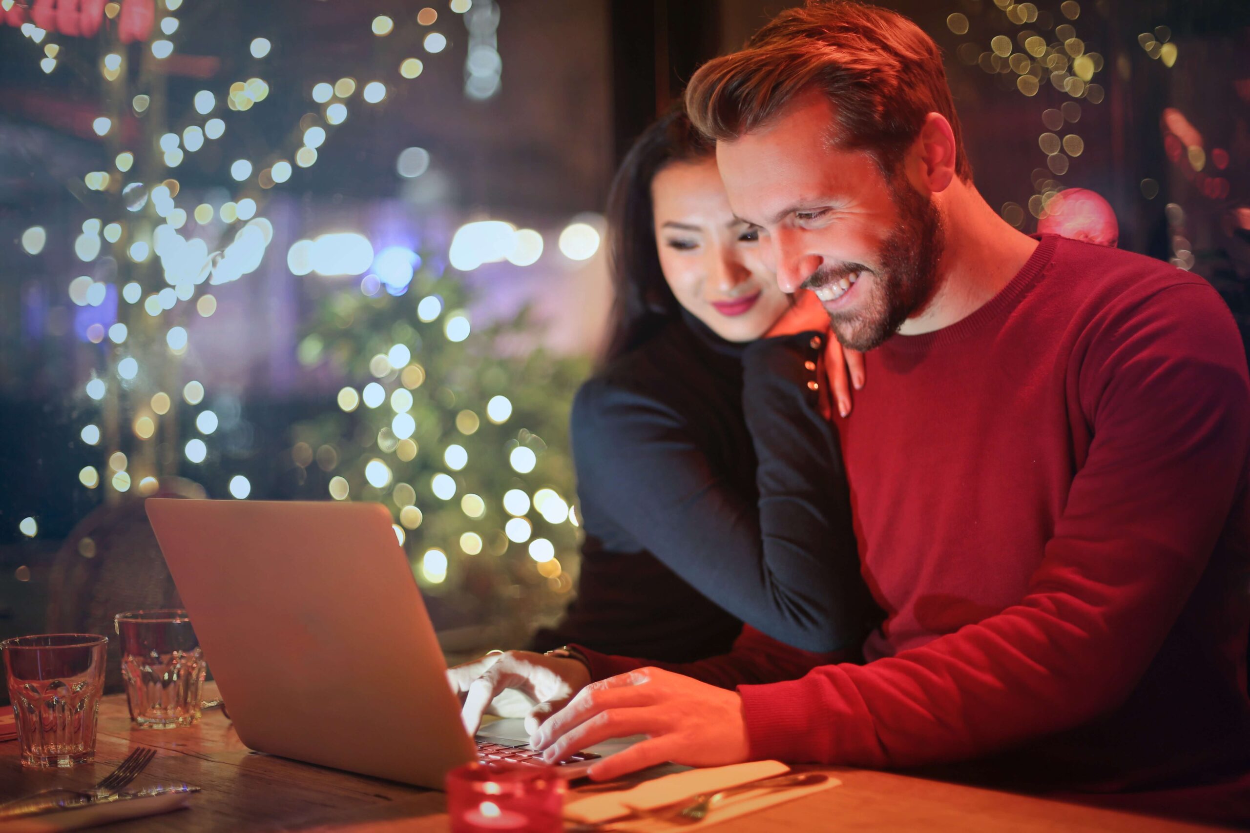 Image of a man and woman smiling and using a laptop. Overcome your relationship issues with the help of couples therapy in Miami, FL.