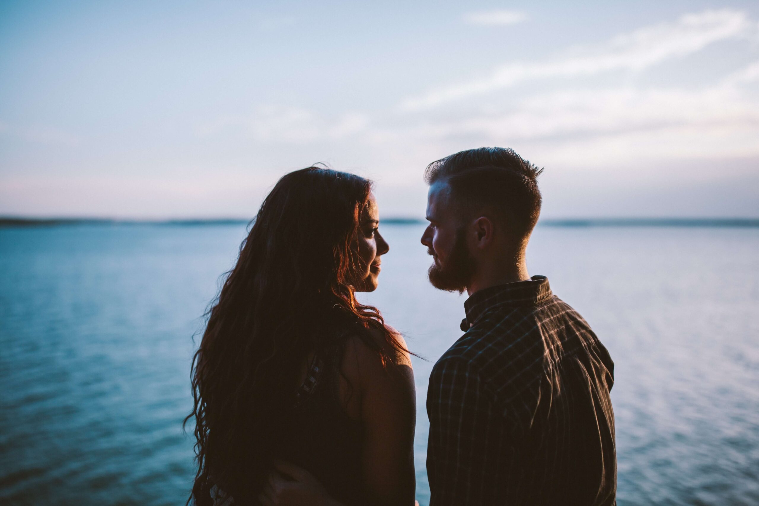 Image of a couple standing in front of a lake looking happily at each other. Discover how marriage counseling in Miami, FL can help you work on reconnecting with your partner.