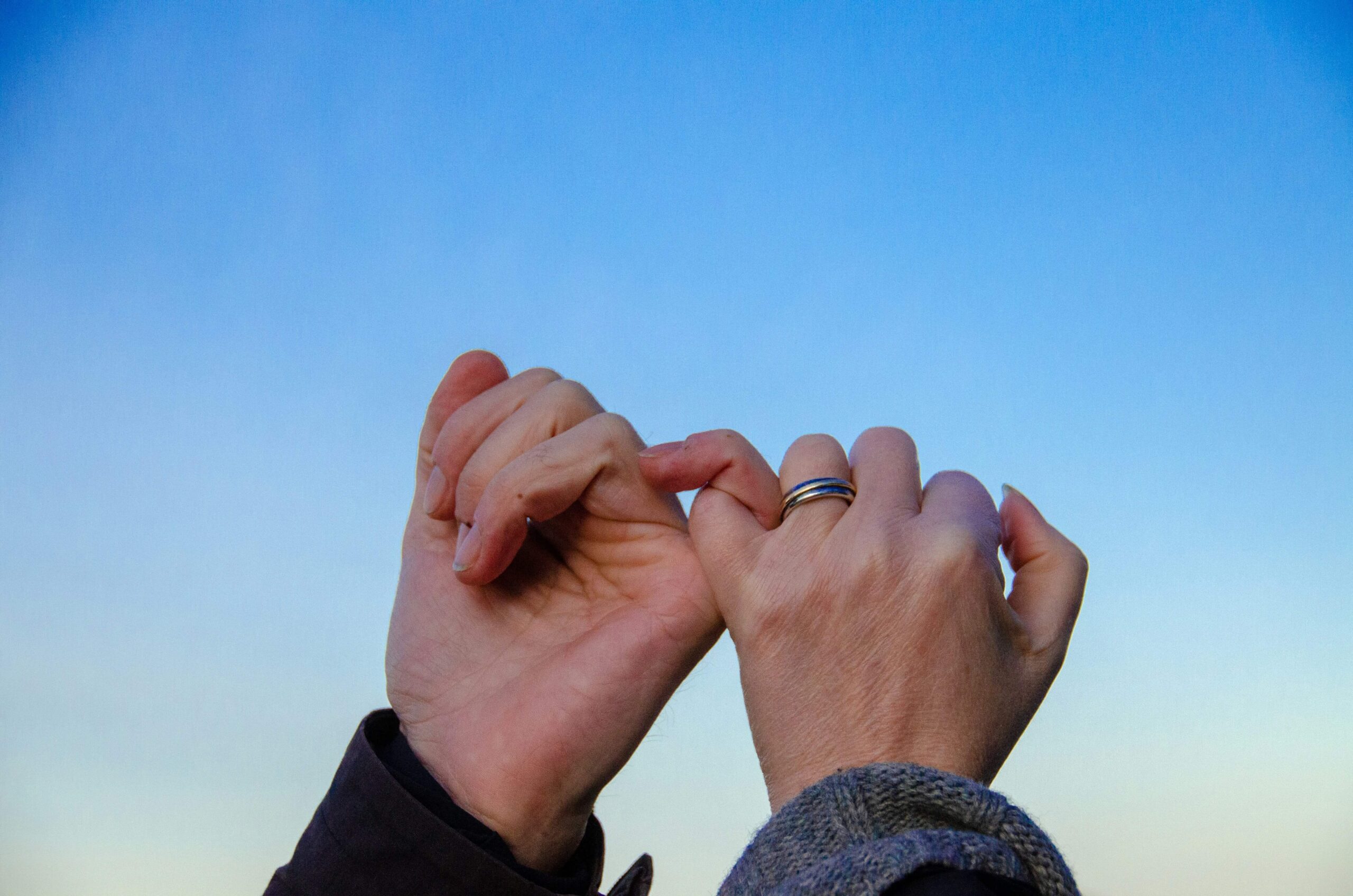 Image of hands holding pinky fingers in front of the blue sky. Work toward rebuilding the trust in your relationship after infidelity with a couples therapist in Miami, FL.