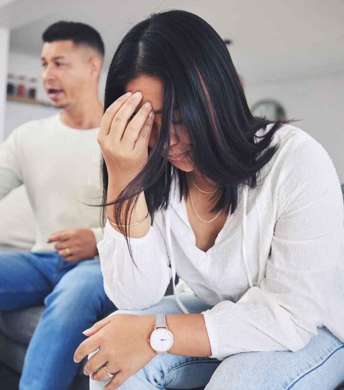 Image of an upset woman sitting on a couch with her partner resting her hand on her forehead. Learn to heal after infidelity with the help of couples therapy in Orlando, FL.