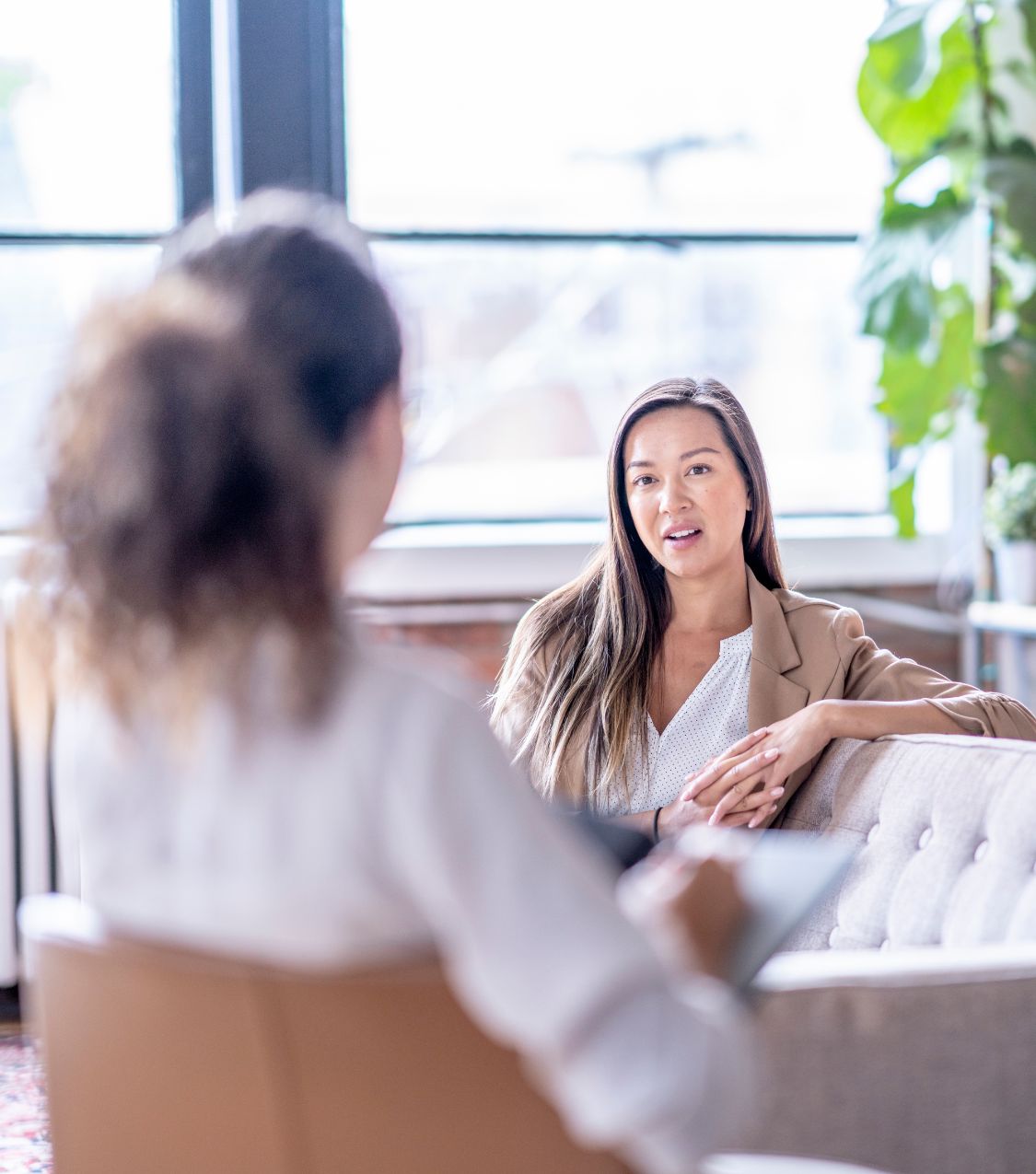 Image of a woman sitting on a couch speaking with a woman sitting in a chair. Discover how you can overcome infidelity with the help of couples therapy in Miami, FL.