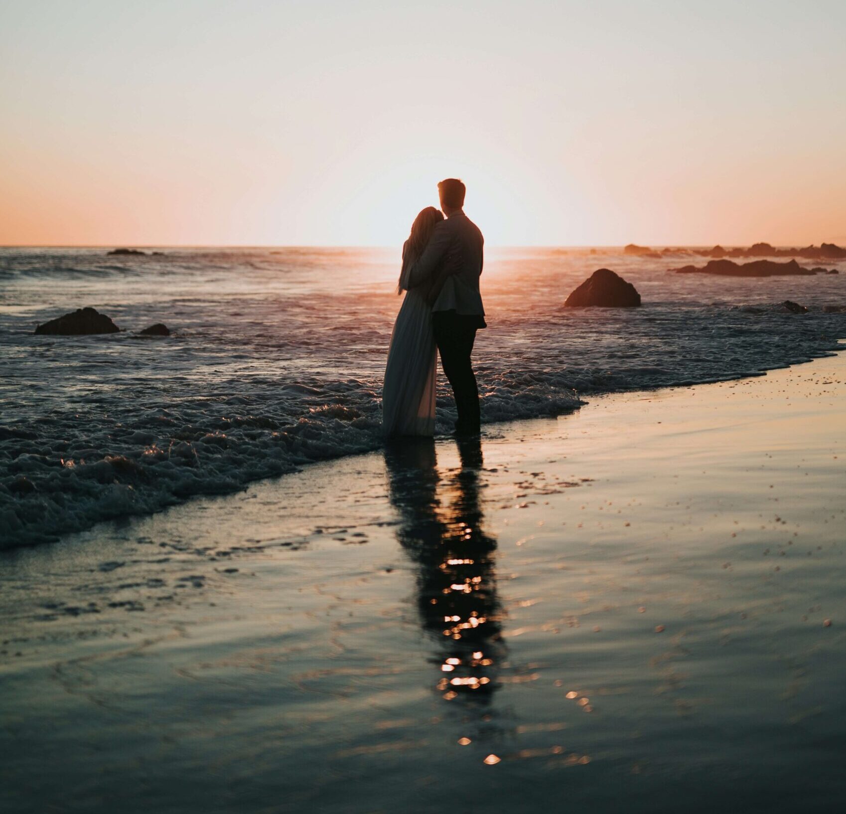 Image of a couple hugging while standing on a beach watching the sun set. Learn to recover from infidelity with affair recovery in Miami, FL to help repair your relationship.