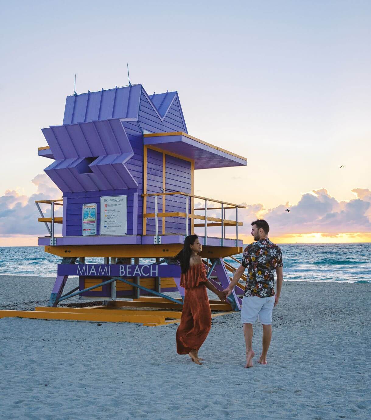 Image of a couple walking on a beach during sunset next to a lifeguard stand. Reconnect with your partner in healthy ways with the help of couples therapy in Miami, FL. Our skilled therapists at Relationship Experts can help you.