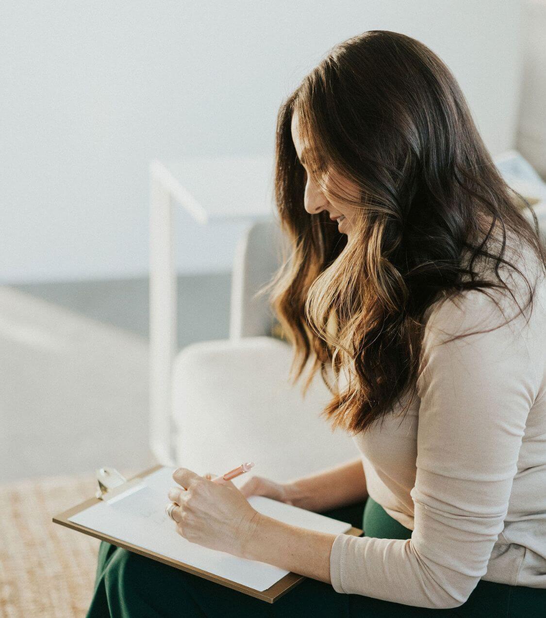 Image of skilled couples therapist Idit Sharoni writing on a clipboard. Work with a couples therapist in Miami, FL who can help you and your partner overcome communication issues.