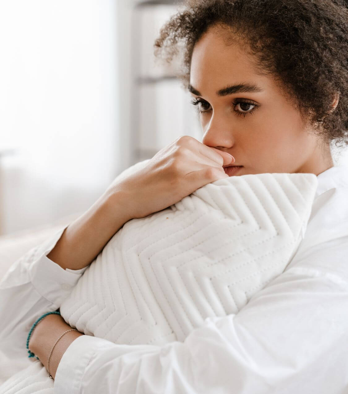 Image of an upset woman sitting on bed holding a pillow to her chest. Begin repairing your relationship after infidelity and reconnecting with your partner with infidelity recovery in Miami, FL.