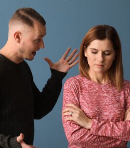 Husband explaining while wife shuts down showing defensive communication patterns after an affair. Woman with closed body language and crossed arms - why wife gets defensive during infidelity recovery. Couples counseling helps break defensive communication in relationships in West Palm Beach Florida. Get help today