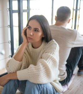 A woman sitting apart from her partner looking distressed after discovering an affair, wondering can my marriage be saved. Marriage counseling can help you know where to start after infidelity. Serving couples in Miami Beach, Tampa, and Orlando. Book your consultation now.