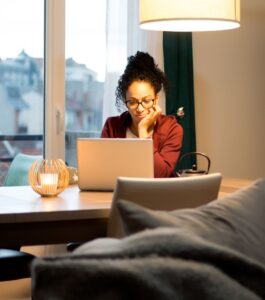 A woman sits alone at a table at home, focused on her laptop screen during an online couples therapy session while her partner is away. Illustrating what couples therapy long distance actually feels like on screen. Online therapy for traveling partners and online therapy while traveling are available for couples in Tampa, Orlando, and Miami Beach. If your partner's travel schedule is affecting your relationship, reach out to Idit Sharoni's Florida couples therapy team today.