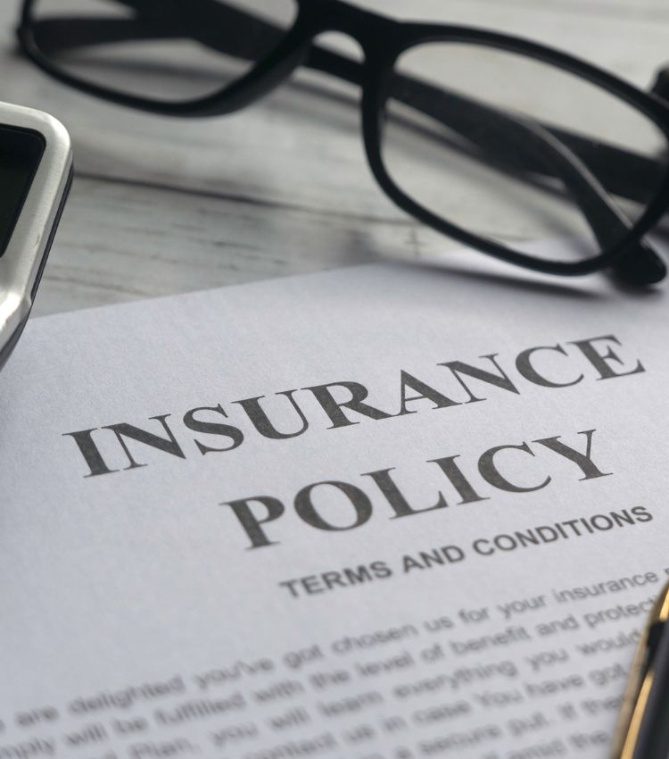 A printed insurance policy with terms and conditions page, with reading glasses and a calculator resting on top. The fine print couples often have to work through when running the math on insurance for couples therapy. This is part of what couples should know before using insurance for marriage counseling, including whether it actually covers couples therapy. For couples in Miami Beach, Tampa, and Orlando. Get the full picture before you compare costs.